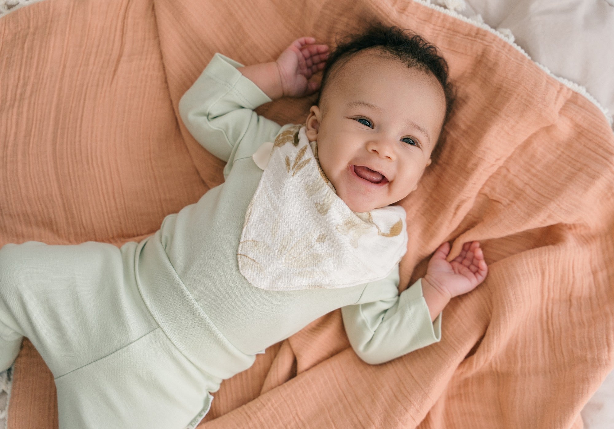 Smiling baby wearing long sleeve bodysuit and fold-over pants in leafy green laying on mat