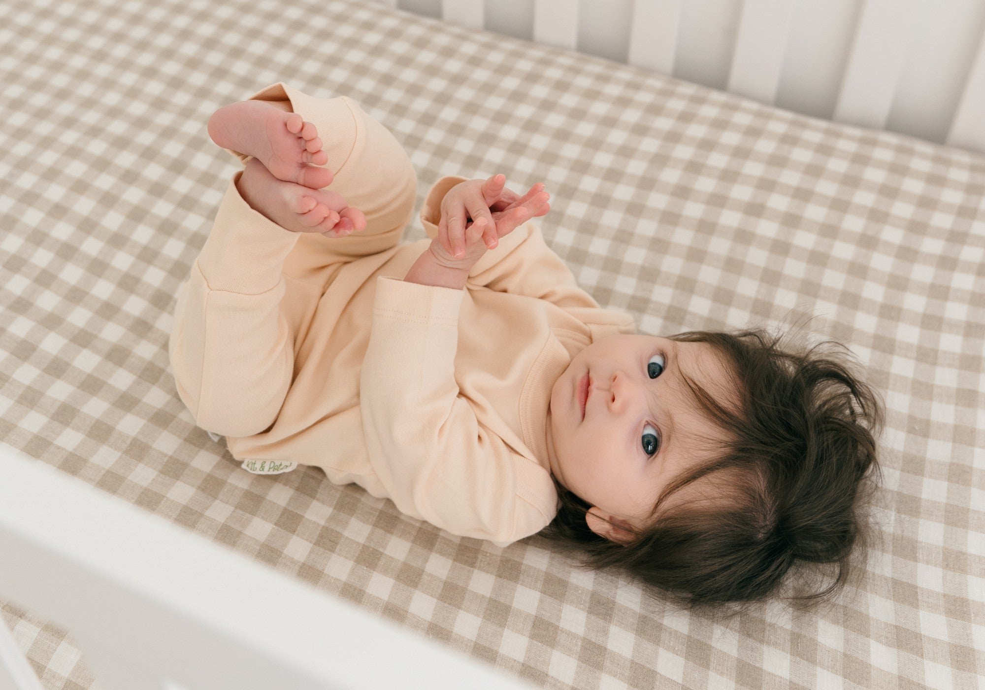 Baby laying in crib wearing long sleeve shirt and fold-over pants in rosy peach