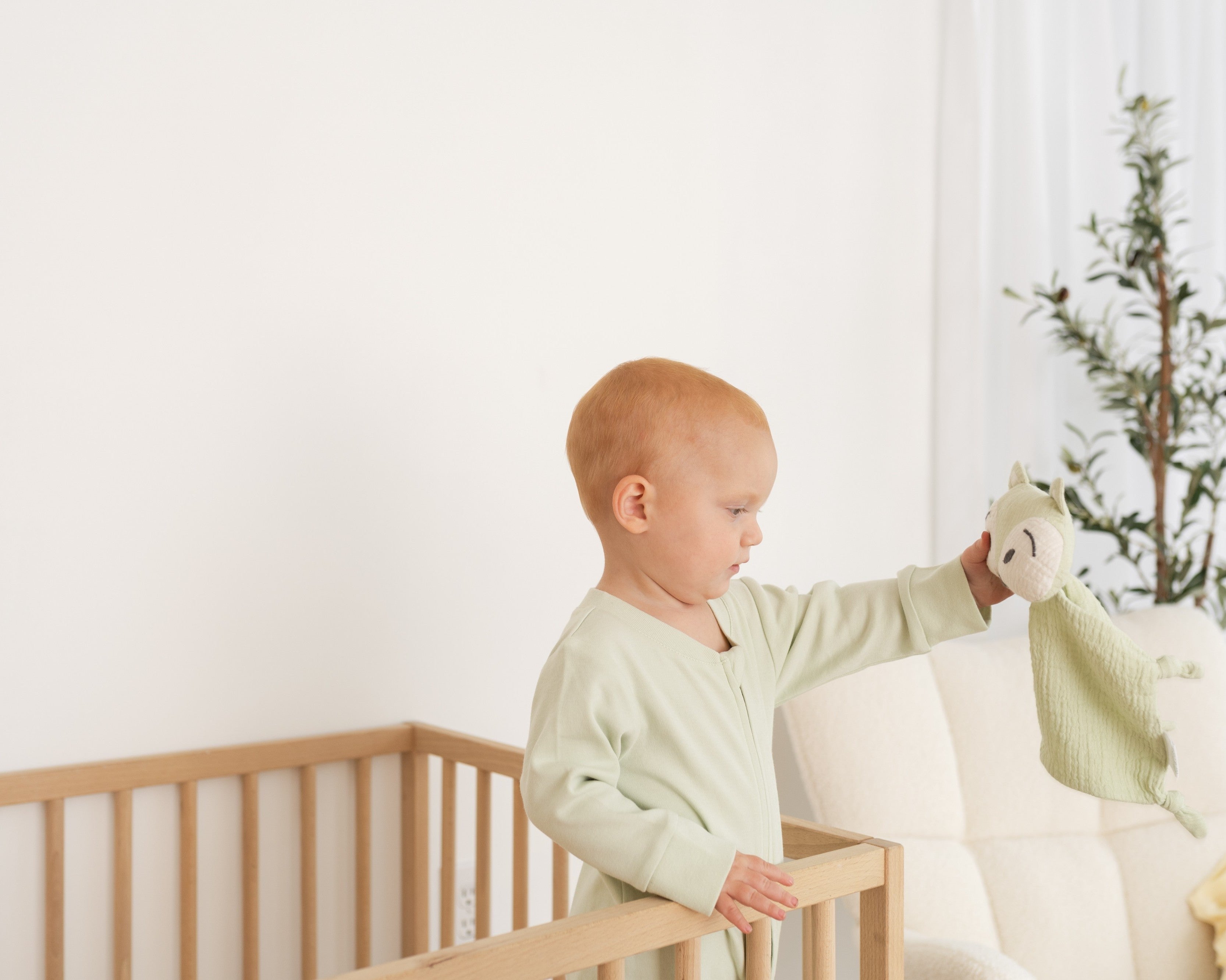 Baby standing in crib holding a fox toy and wearing a Kit & Petal Leafy Green long sleeve romper.