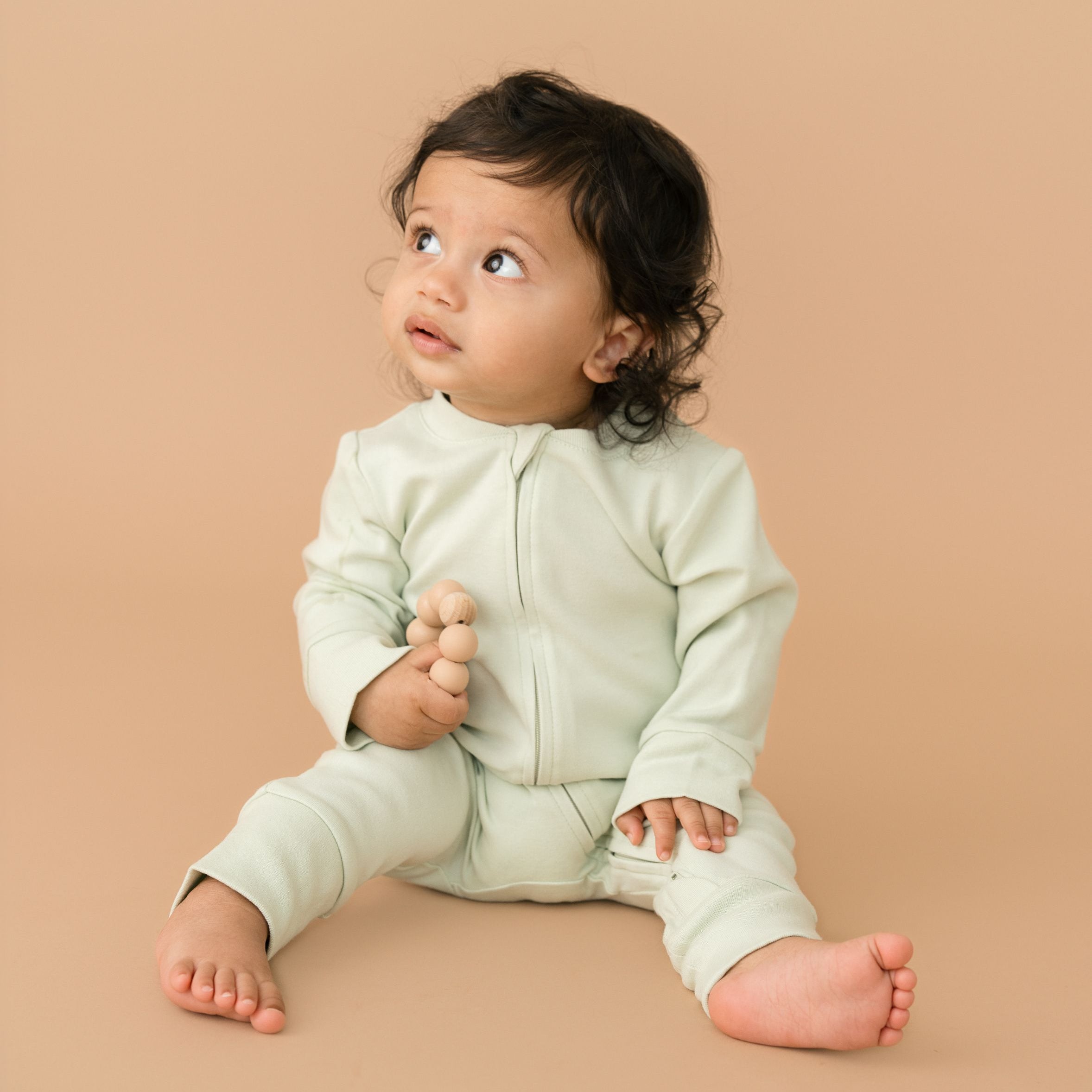Baby boy wearing a Leafy Green organic cotton long sleeve romper, holding a toy.