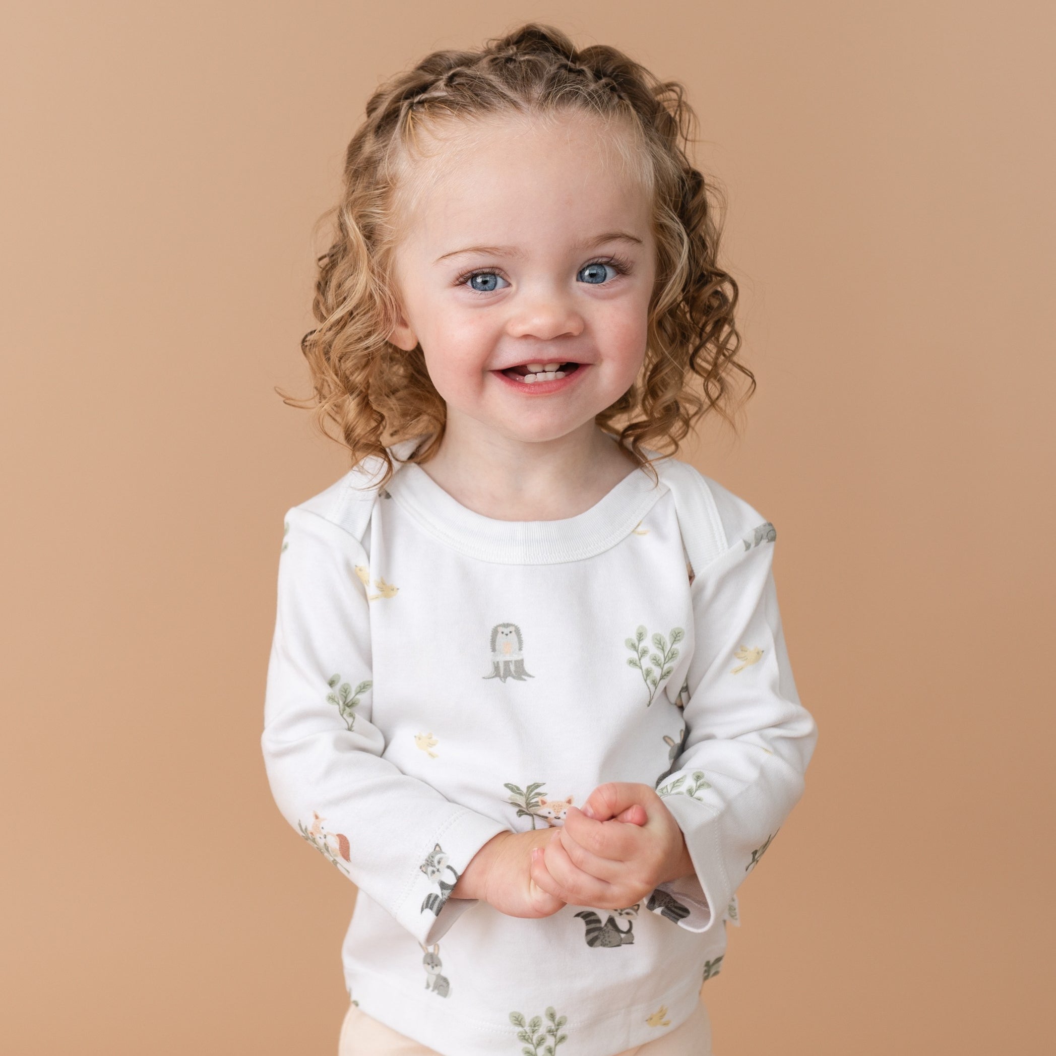 Toddler girl smiling in Forest Friends organic cotton long sleeve shirt and rosy peach fold-over pants