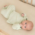 Baby lying in crib wearing leafy green organic cotton long sleeve shirt and fold-over pants