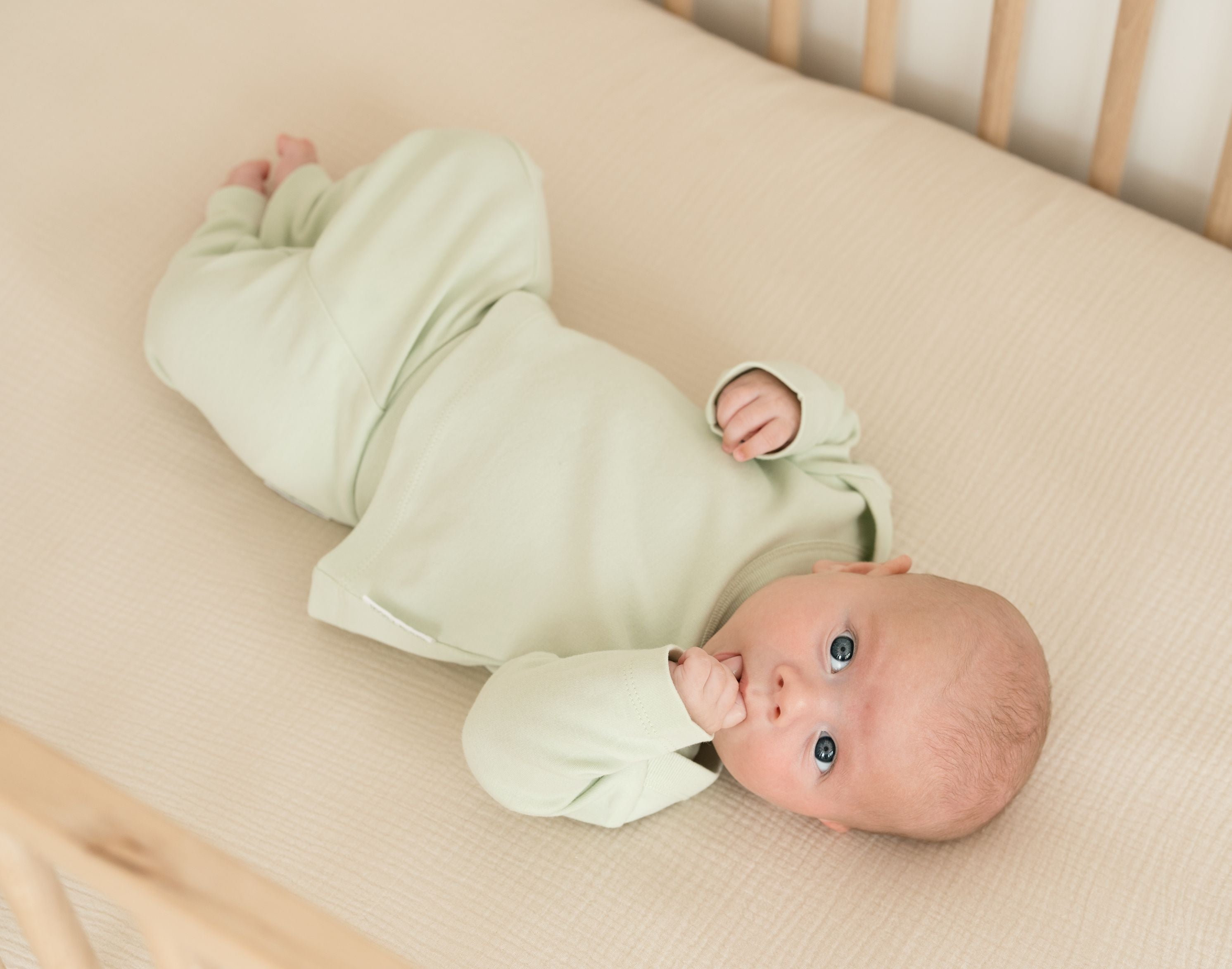 Baby lying in crib wearing leafy green organic cotton long sleeve shirt and fold-over pants