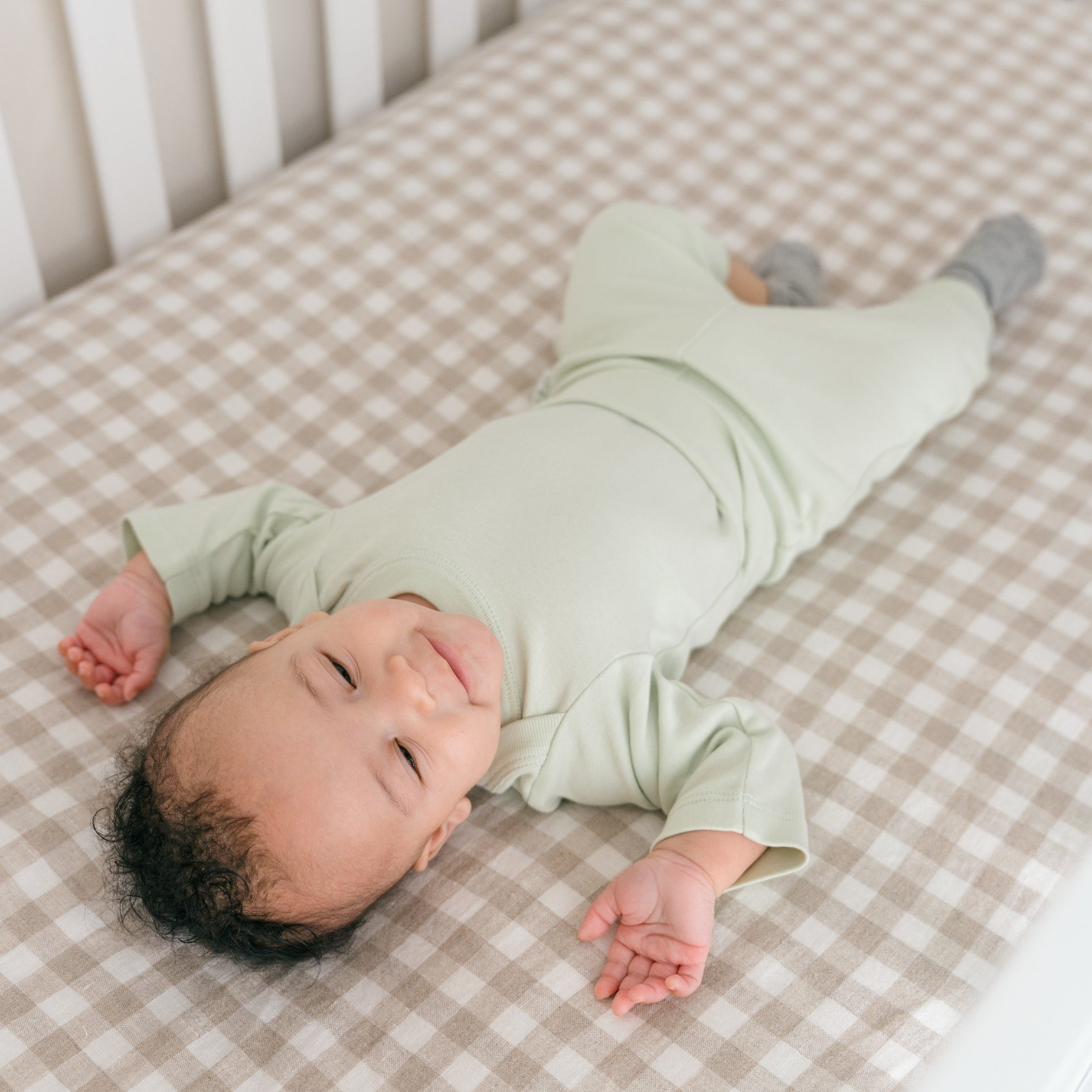 Baby boy wearing a Leafy Green organic cotton long sleeve bodysuit and fold-over pants, laying in a crib.