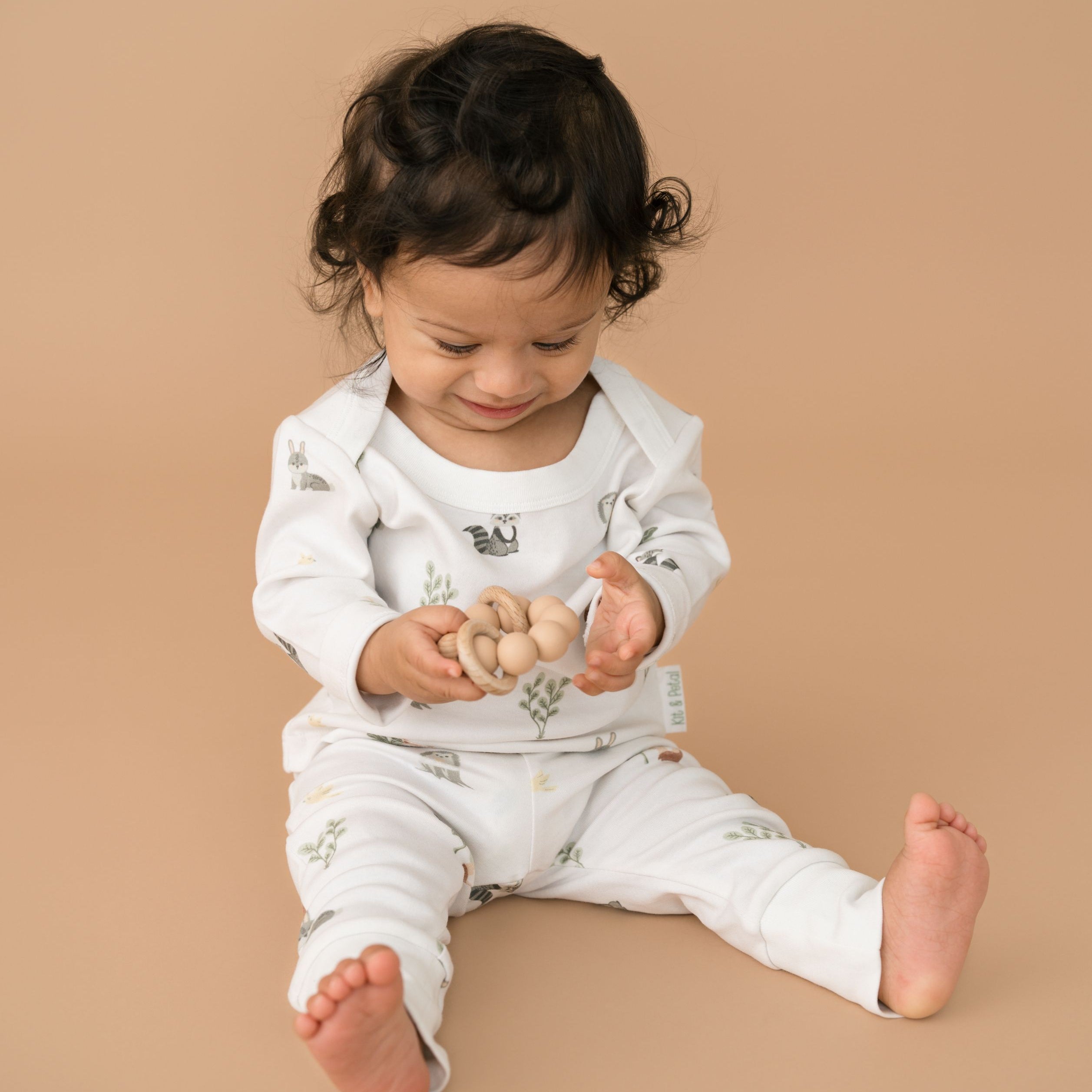 Baby holding a toy and wearing forest friends organic cotton fold-over pants and matching long sleeve shirt