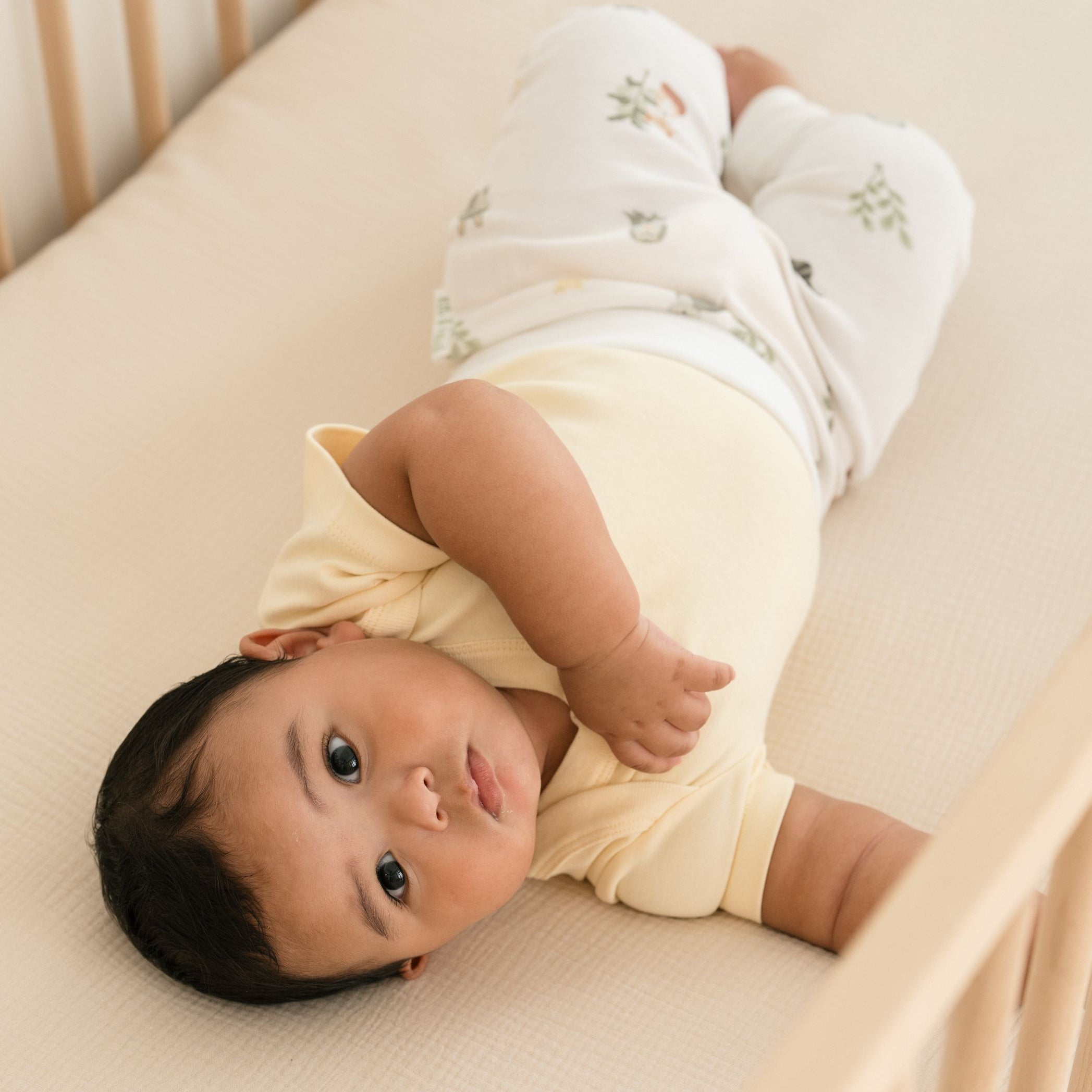 Baby lying in crib wearing forest friends organic cotton fold-over pants and sunny yellow short sleeve bodysuit