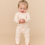 Toddler girl in a Rosy Peach long sleeve romper made from soft organic cotton, holding a ball toy.