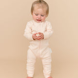 Toddler girl in a Rosy Peach long sleeve romper made from soft organic cotton, holding a ball toy.