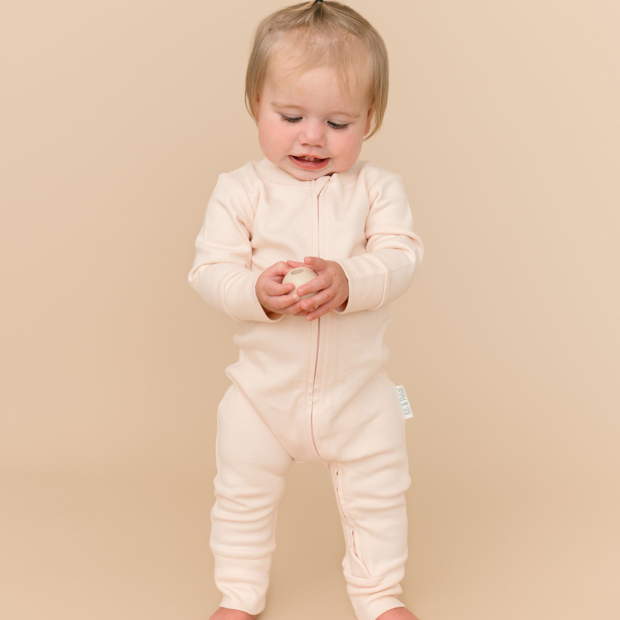Toddler girl in a Rosy Peach long sleeve romper made from soft organic cotton, holding a ball toy.
