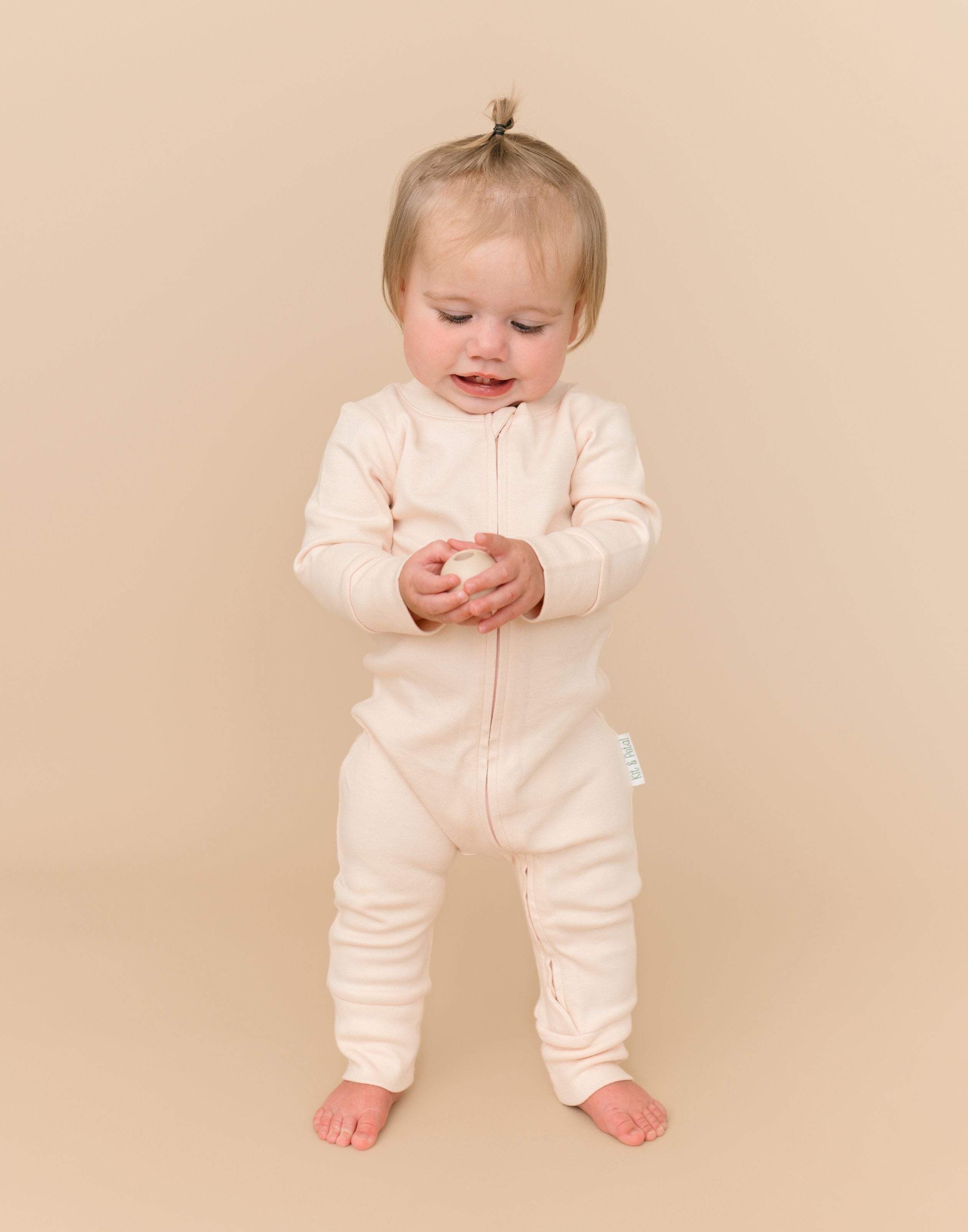 Toddler girl in a Rosy Peach long sleeve romper made from soft organic cotton, holding a ball toy.