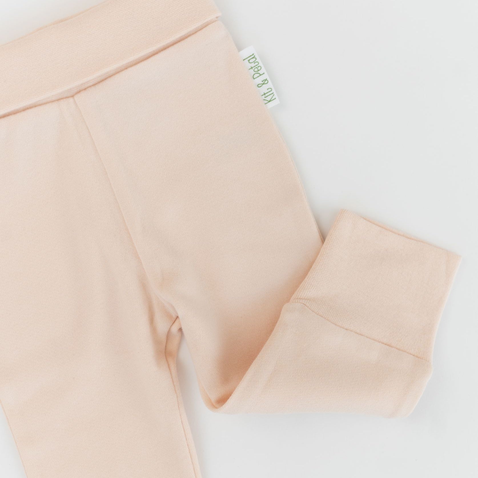 Close-up of soft, wide waistband and hem details on rosy peach organic cotton baby fold-over pants