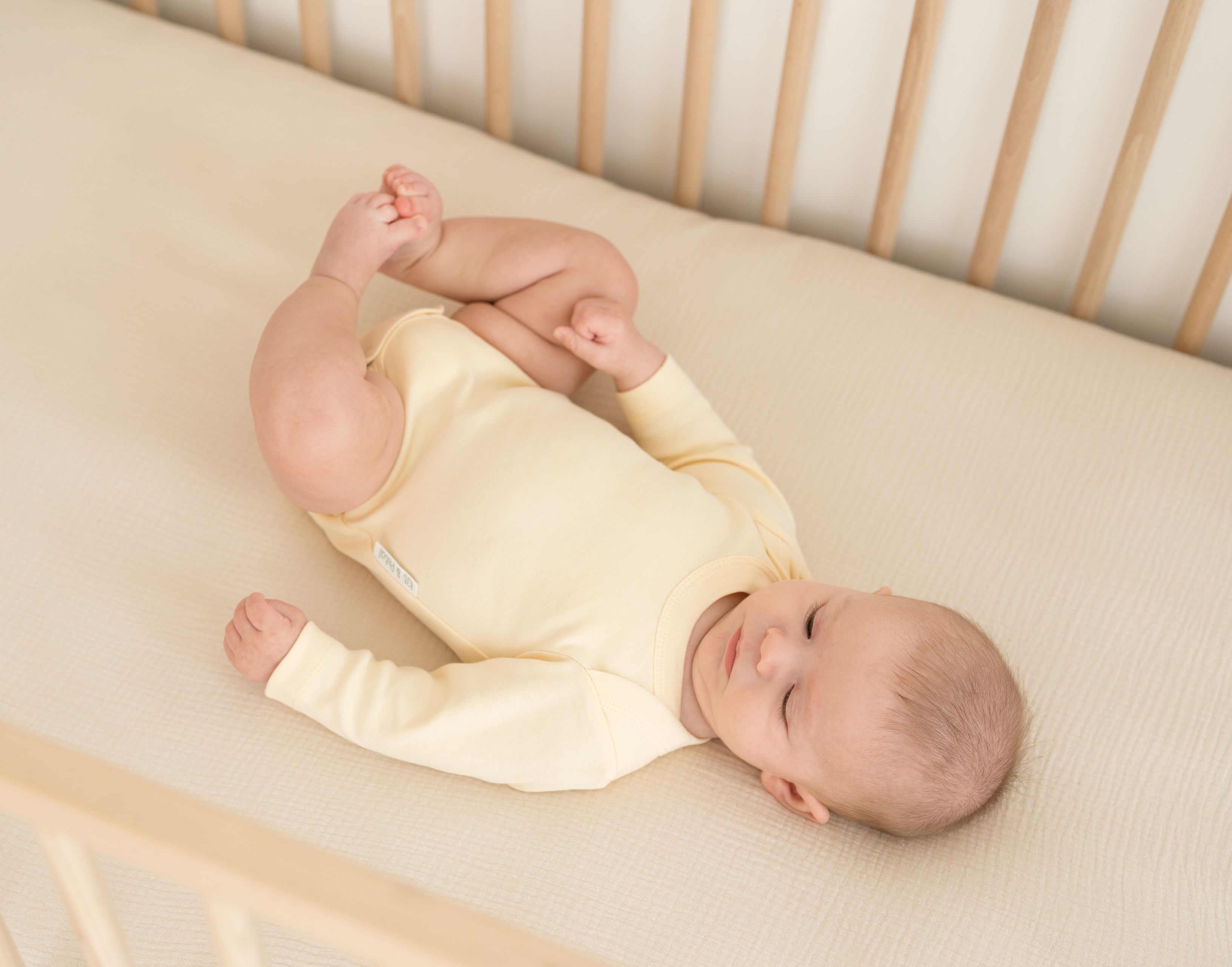 Baby wearing a Sunny Yellow organic cotton long sleeve bodysuit, laying in a crib.