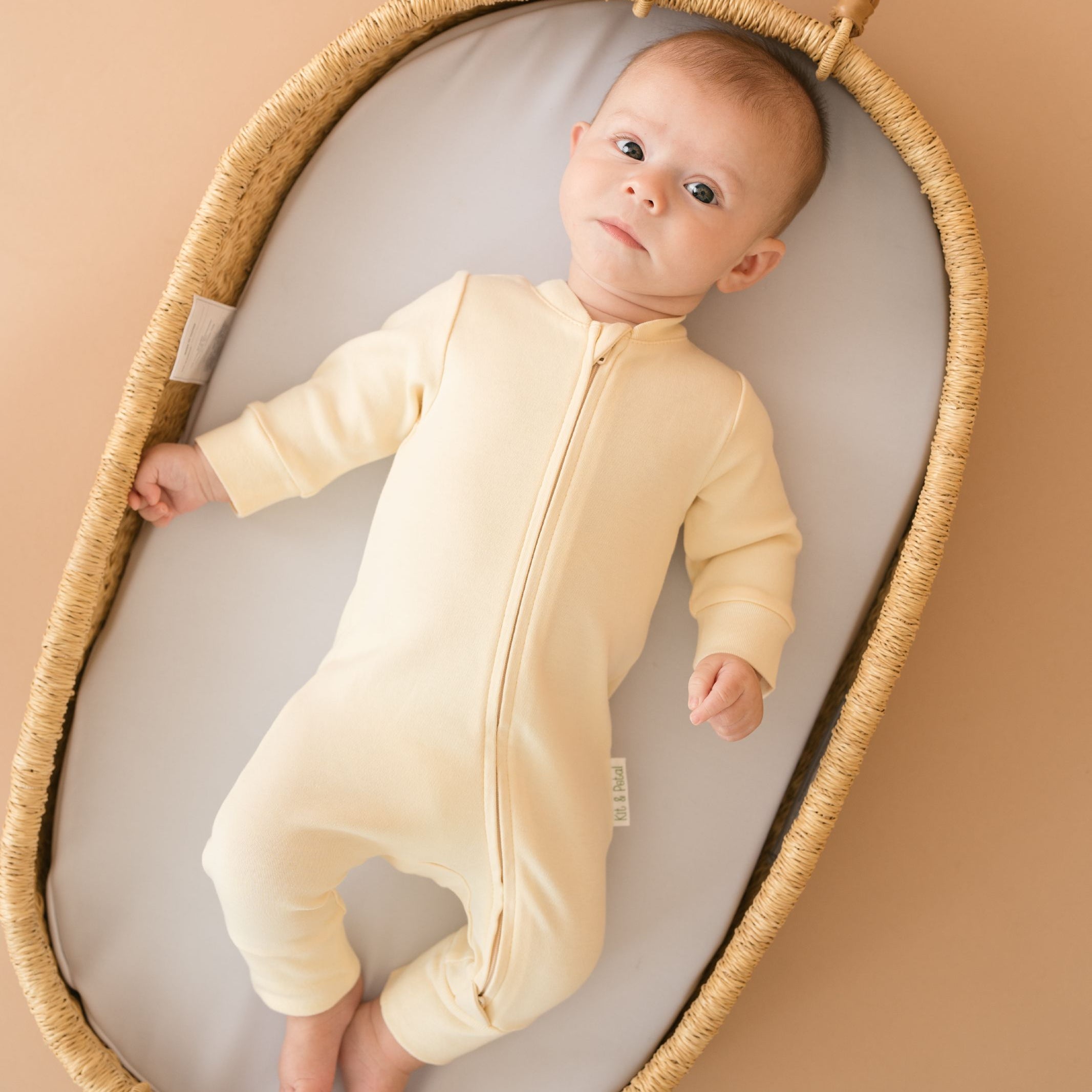 Baby wearing a Sunny Yellow organic cotton long sleeve romper, laying in a bassinet.