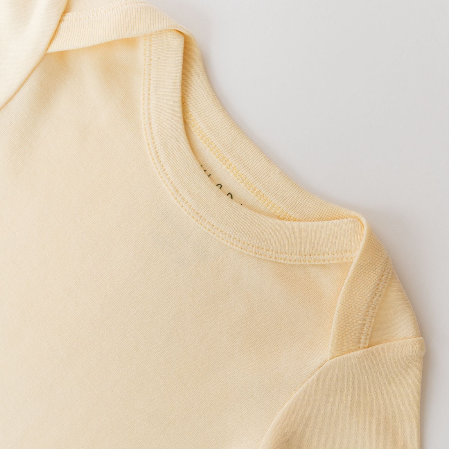 Close-up of envelope neckline on sunny yellow organic cotton baby long sleeve shirt