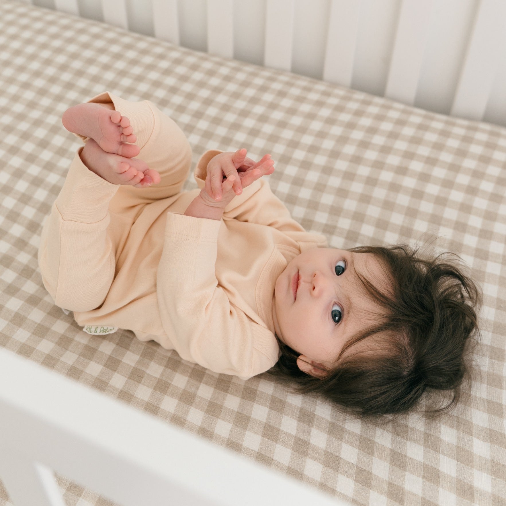 Baby lying in crib wearing rosy peach organic cotton long sleeve shirt and fold-over pants