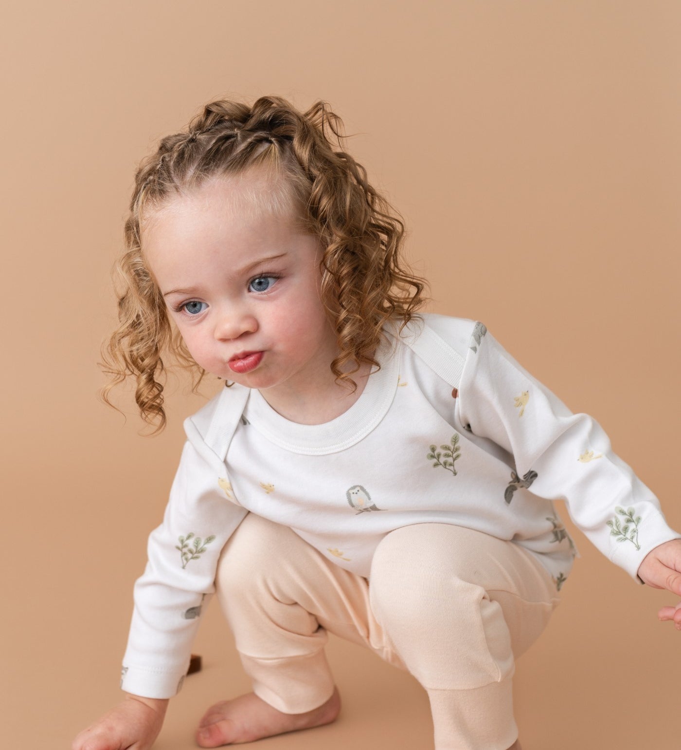 Toddler girl wearing long sleeve shirt in forest friends animal print and fold-over pants in rosy peach color