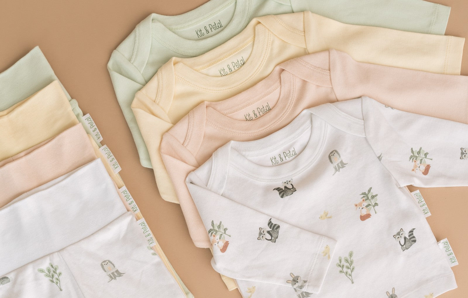 Flat lay of Kit & Petal long sleeve shirts and fold over pants in all four colorways, including forest friends animal print, rosy peach, sunny yellow and leafy green