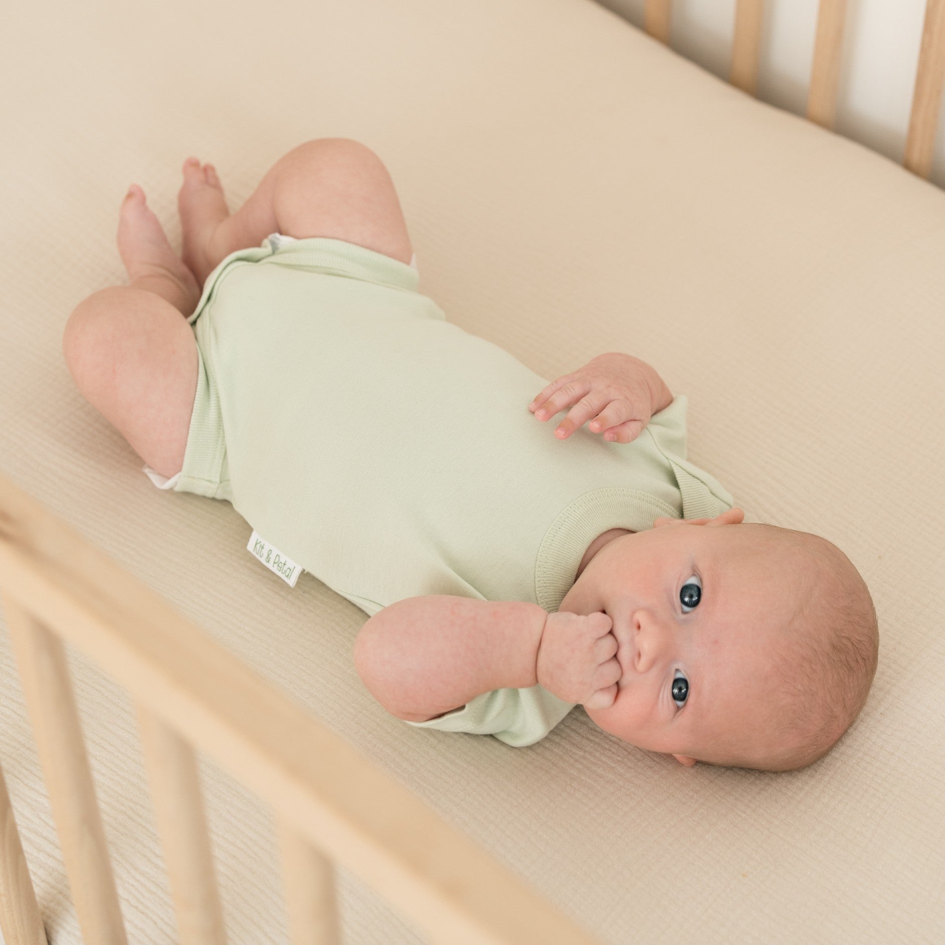 Baby laying in crib wearing a leafy green Kit & Petal bodysuit in short sleeve