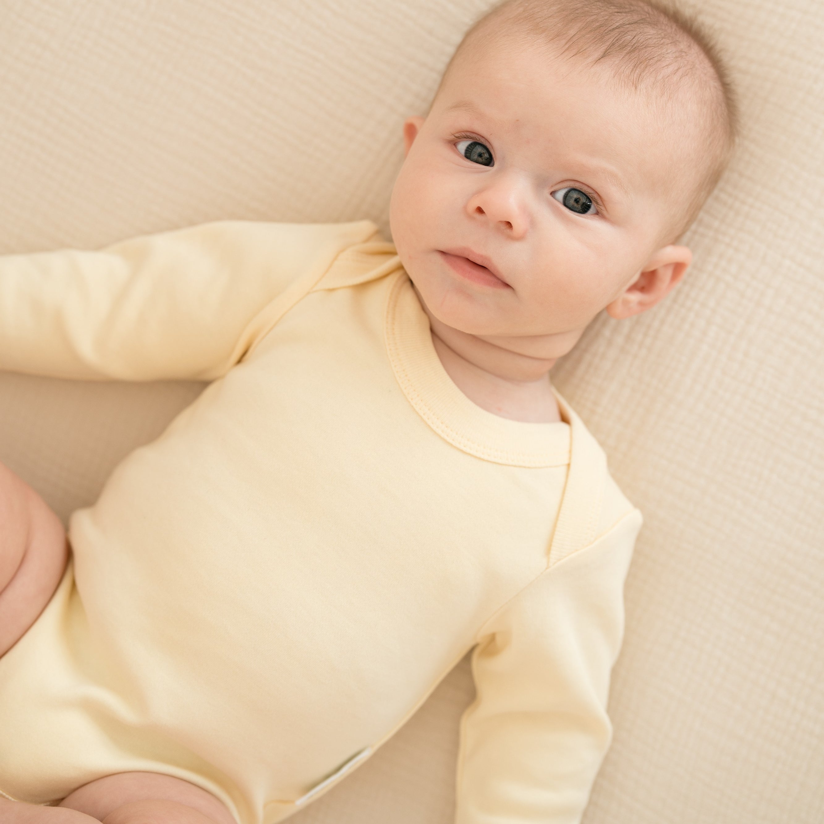 Baby laying in crib wearing a long sleeve bodysuit in Sunny Yellow color