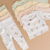 A stack of four long sleeve shirts in four different colorways, and a stack of four fold-over pants in four different colorways. Forest friends animal print, rosy peach, sunny yellow and leafy green.