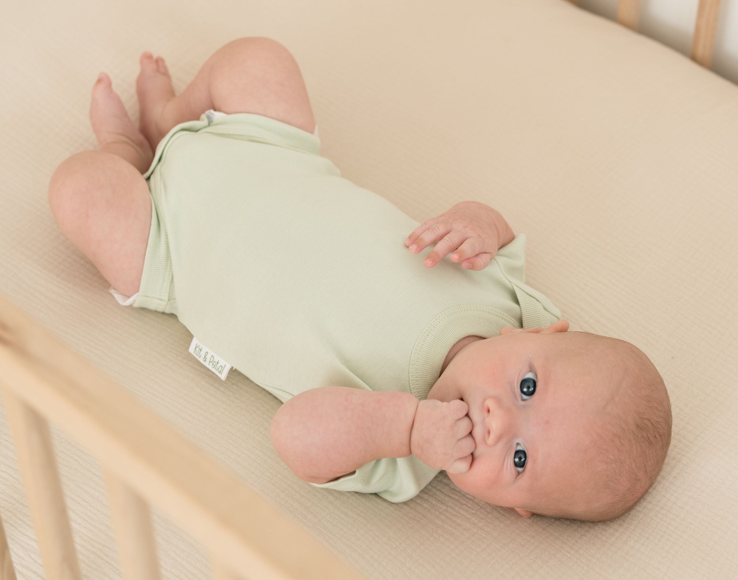 Baby in crib wearing a Leafy Green organic cotton short sleeve bodysuit.