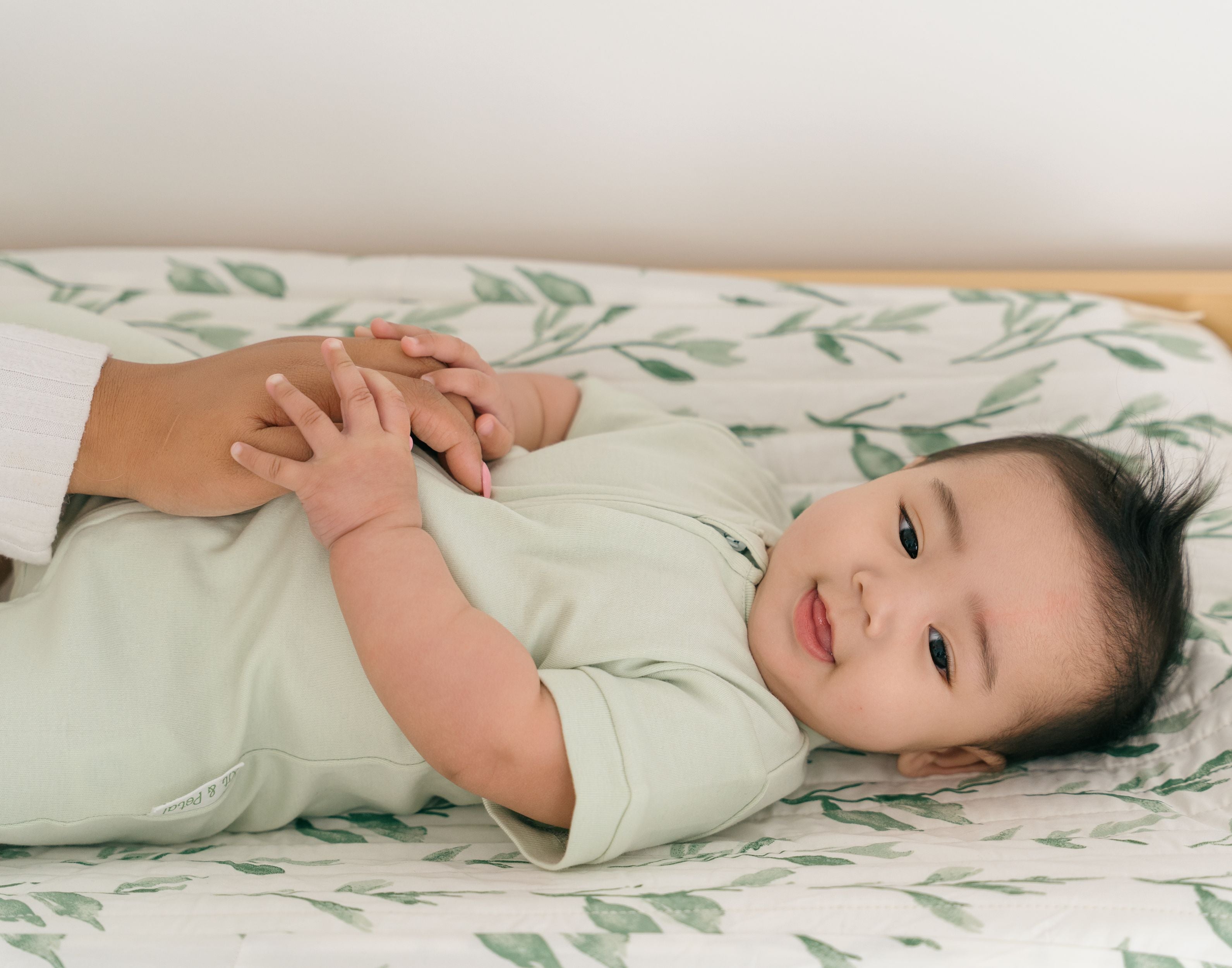 Baby smiling while laying on a changing table wearing a Leafy Green organic cotton short sleeve romper.