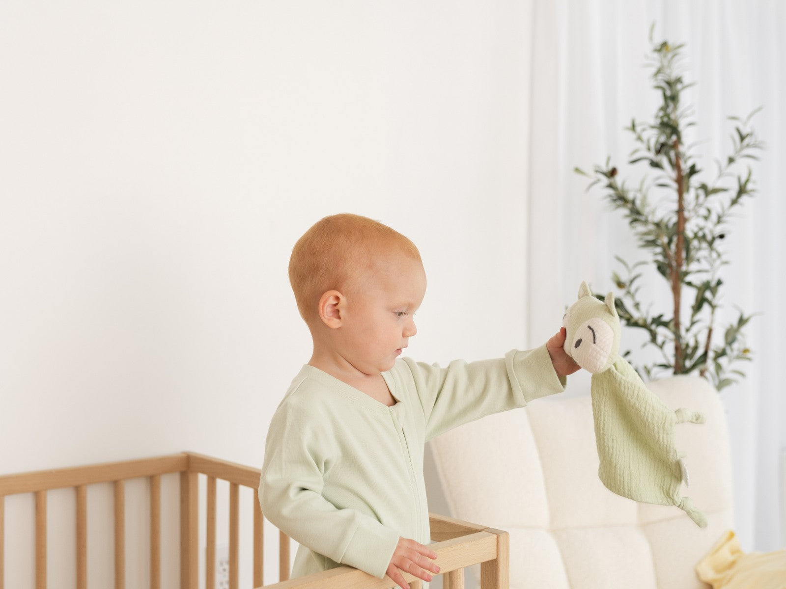 Baby wearing long sleeve romper in leafy green holding a fox toy.