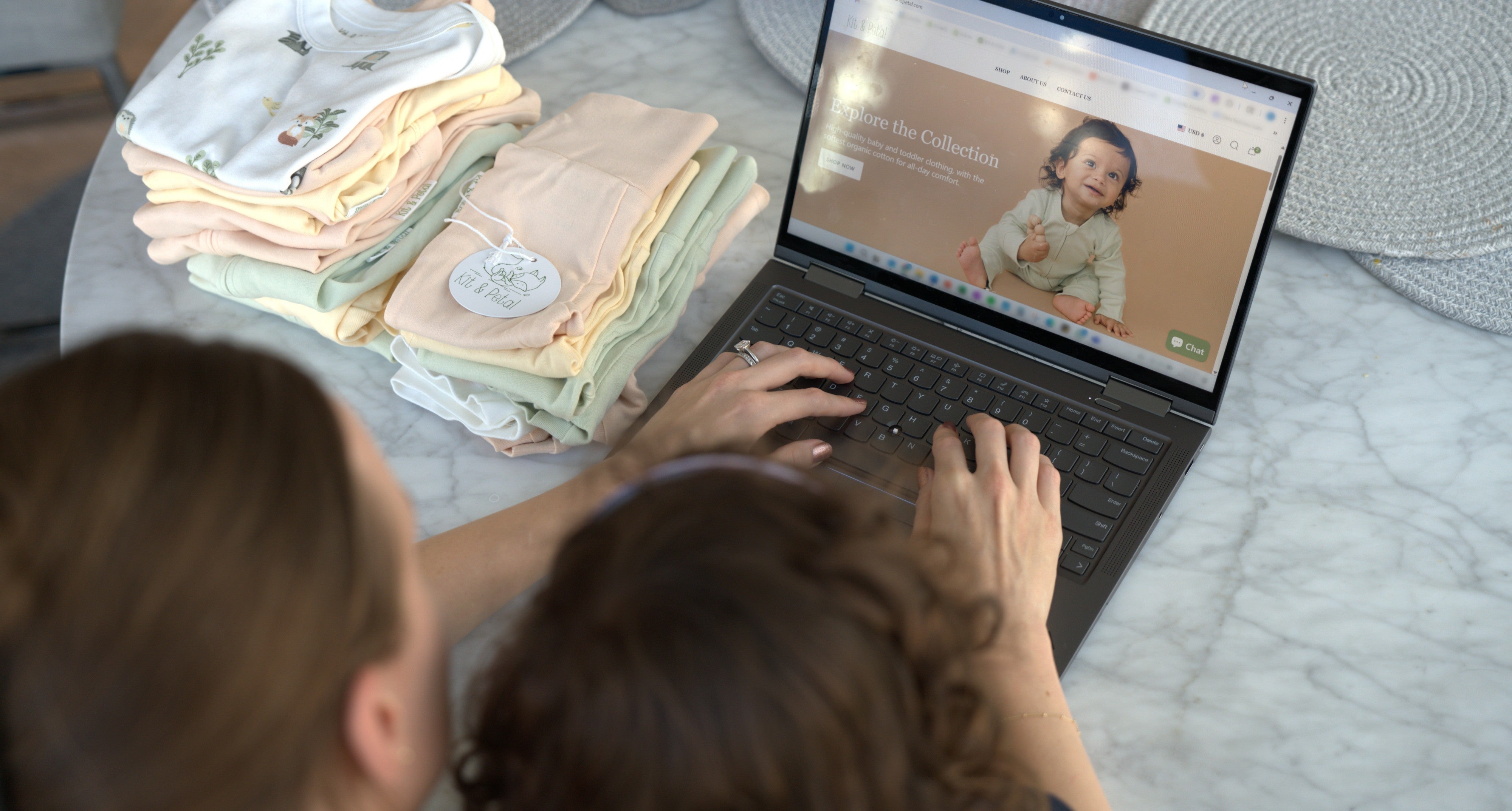 Founder of Kit & Petal using a laptop with baby clothes on a table