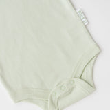 Close-up of snap buttons and Kit & Petal brand label on leafy green organic cotton baby short sleeve bodysuit