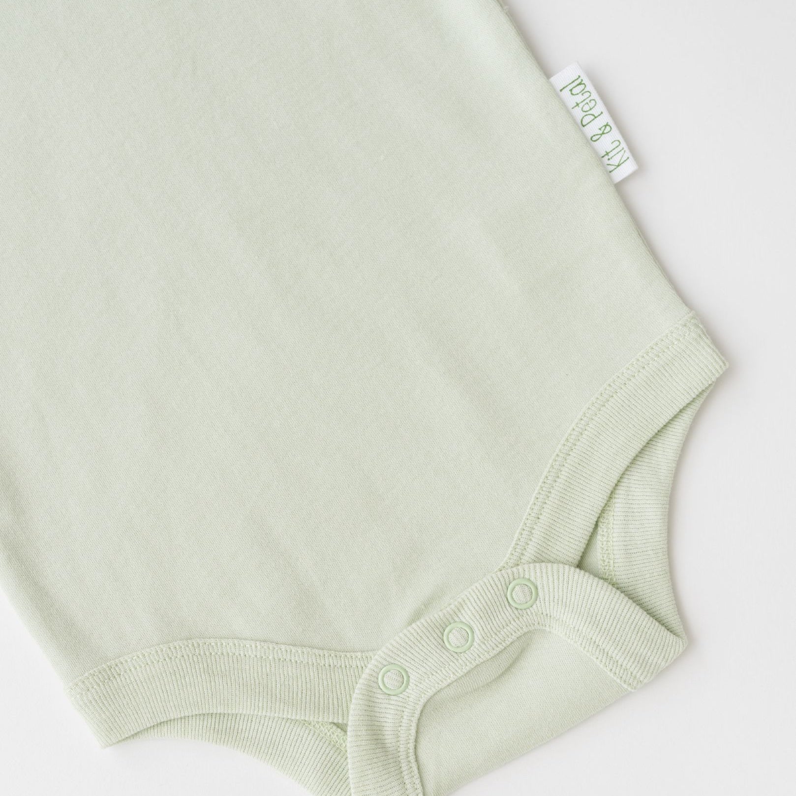 Close-up of snap buttons and Kit & Petal brand label on leafy green organic cotton baby short sleeve bodysuit