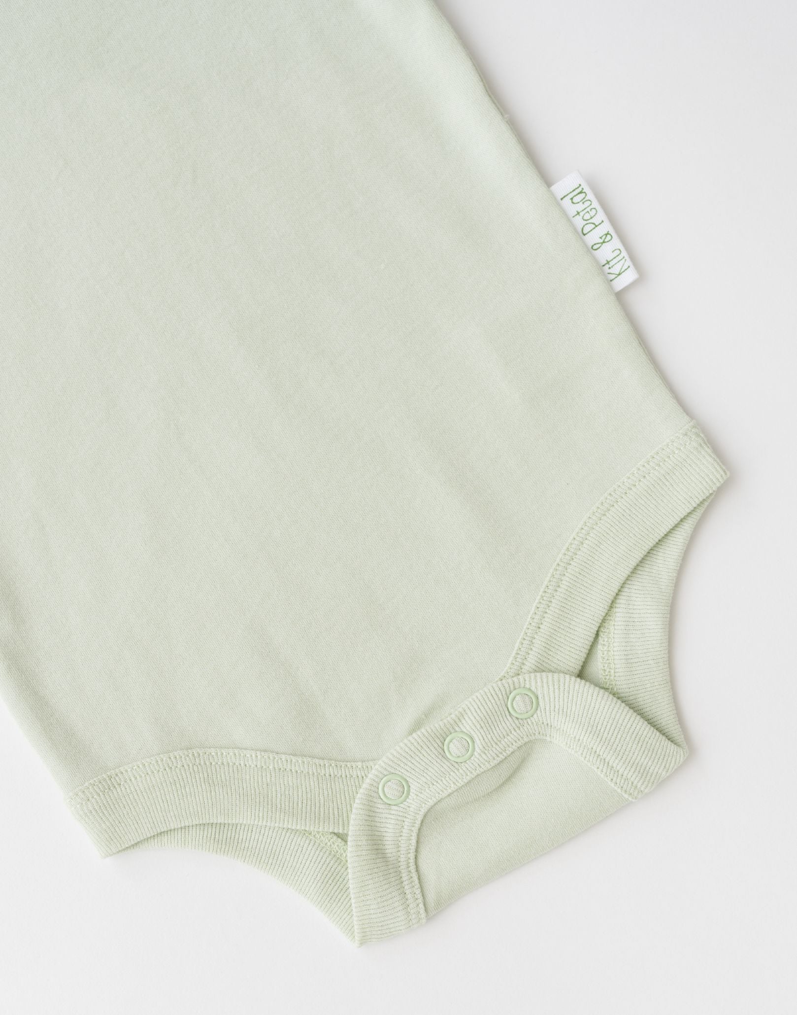 Close-up of snap buttons and Kit & Petal brand label on leafy green organic cotton baby short sleeve bodysuit