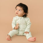 Baby wearing leafy green organic cotton long sleeve romper, holding a toy