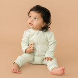 Baby wearing leafy green organic cotton long sleeve romper, holding a toy