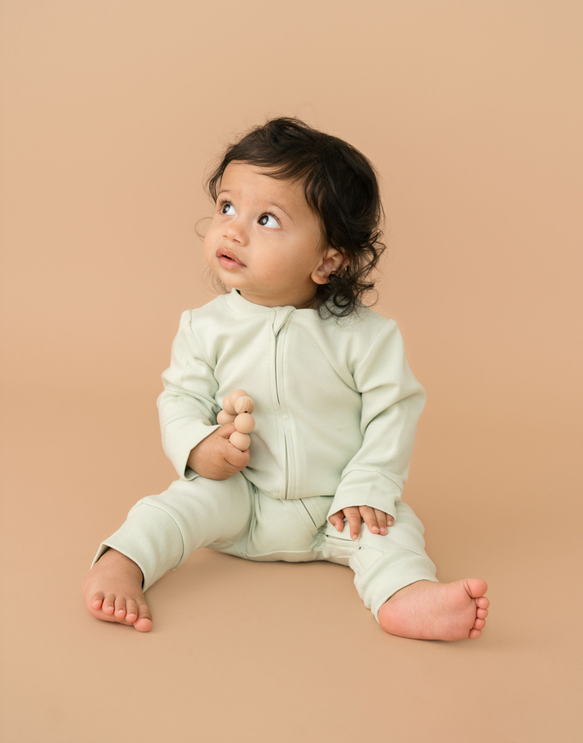 Baby wearing leafy green organic cotton long sleeve romper, holding a toy
