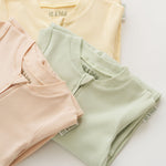 Stack of organic cotton baby long sleeve rompers in leafy green, rosy peach, and sunny yellow, with leafy green in focus