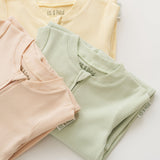 Stack of organic cotton baby long sleeve rompers in leafy green, rosy peach, and sunny yellow, with leafy green in focus