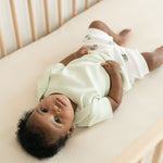 Baby laying in a crib wearing a Leafy Green organic cotton short sleeve shirt and Forest Friends print fold-over shorts.