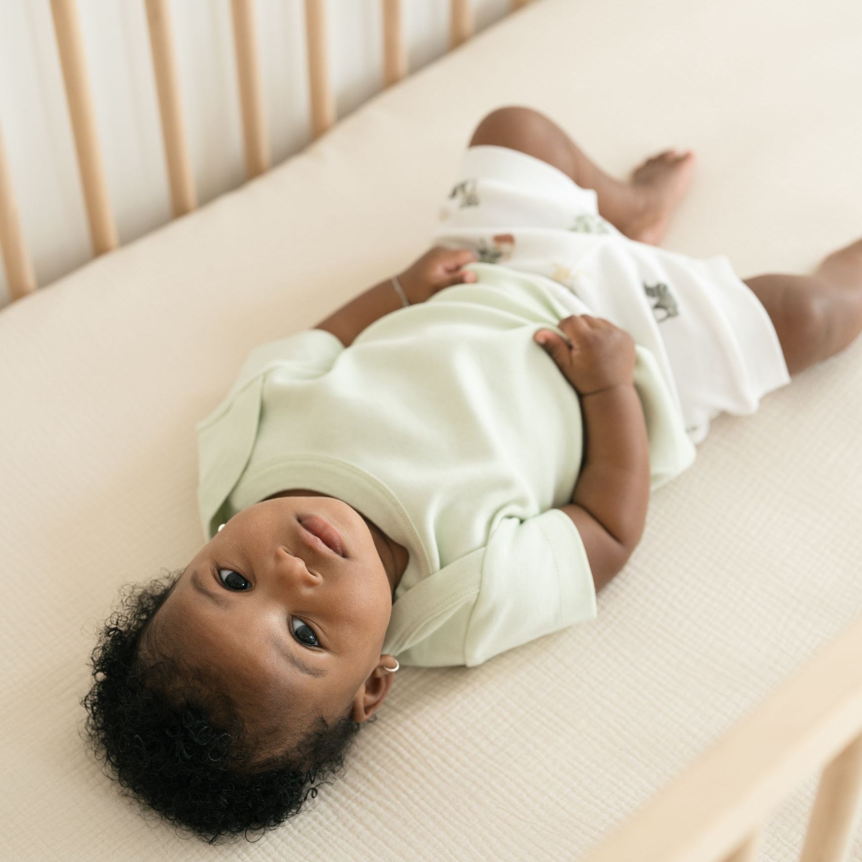 Baby laying in a crib wearing a Leafy Green organic cotton short sleeve shirt and Forest Friends print fold-over shorts.