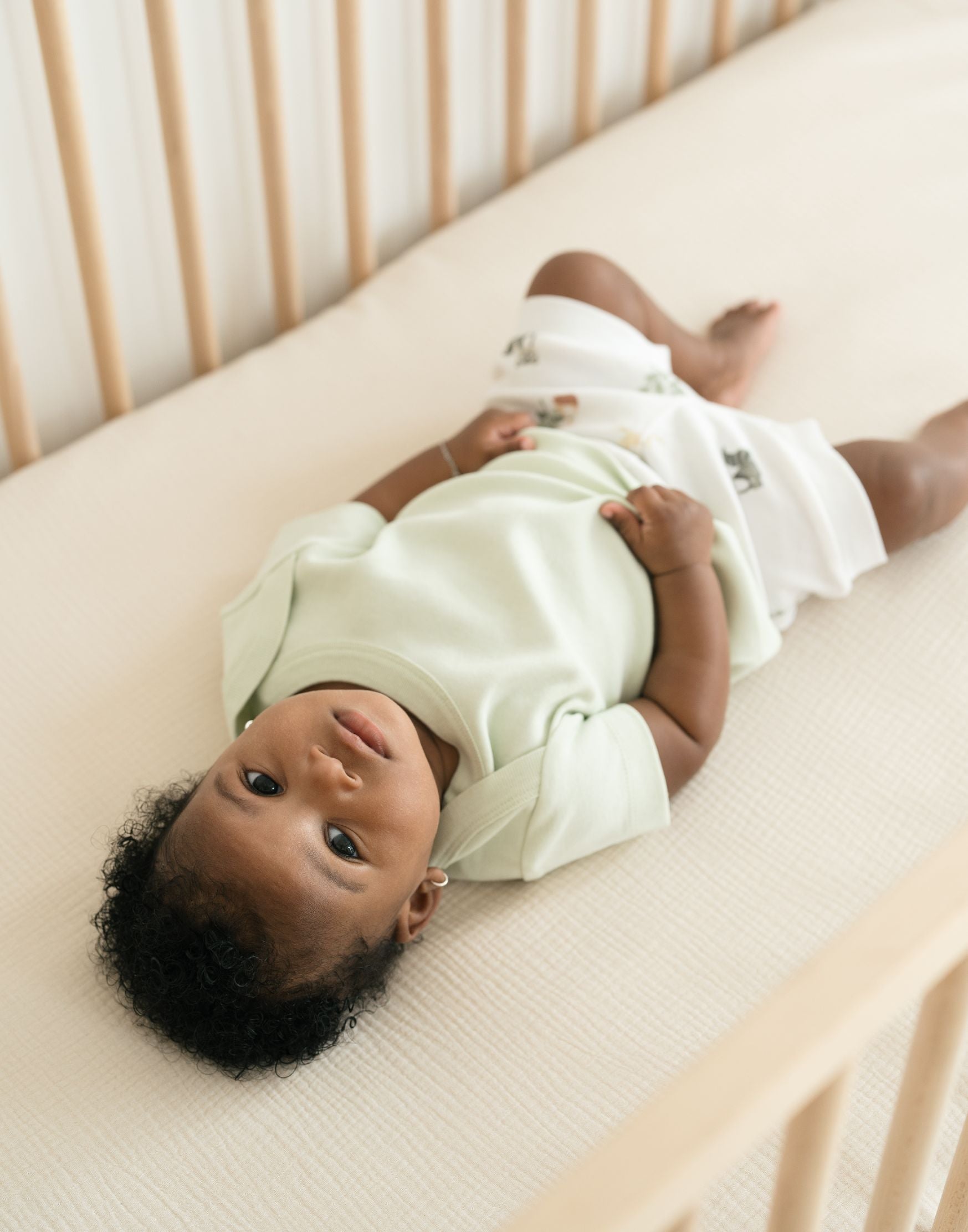 Baby laying in a crib wearing a Leafy Green organic cotton short sleeve shirt and Forest Friends print fold-over shorts.