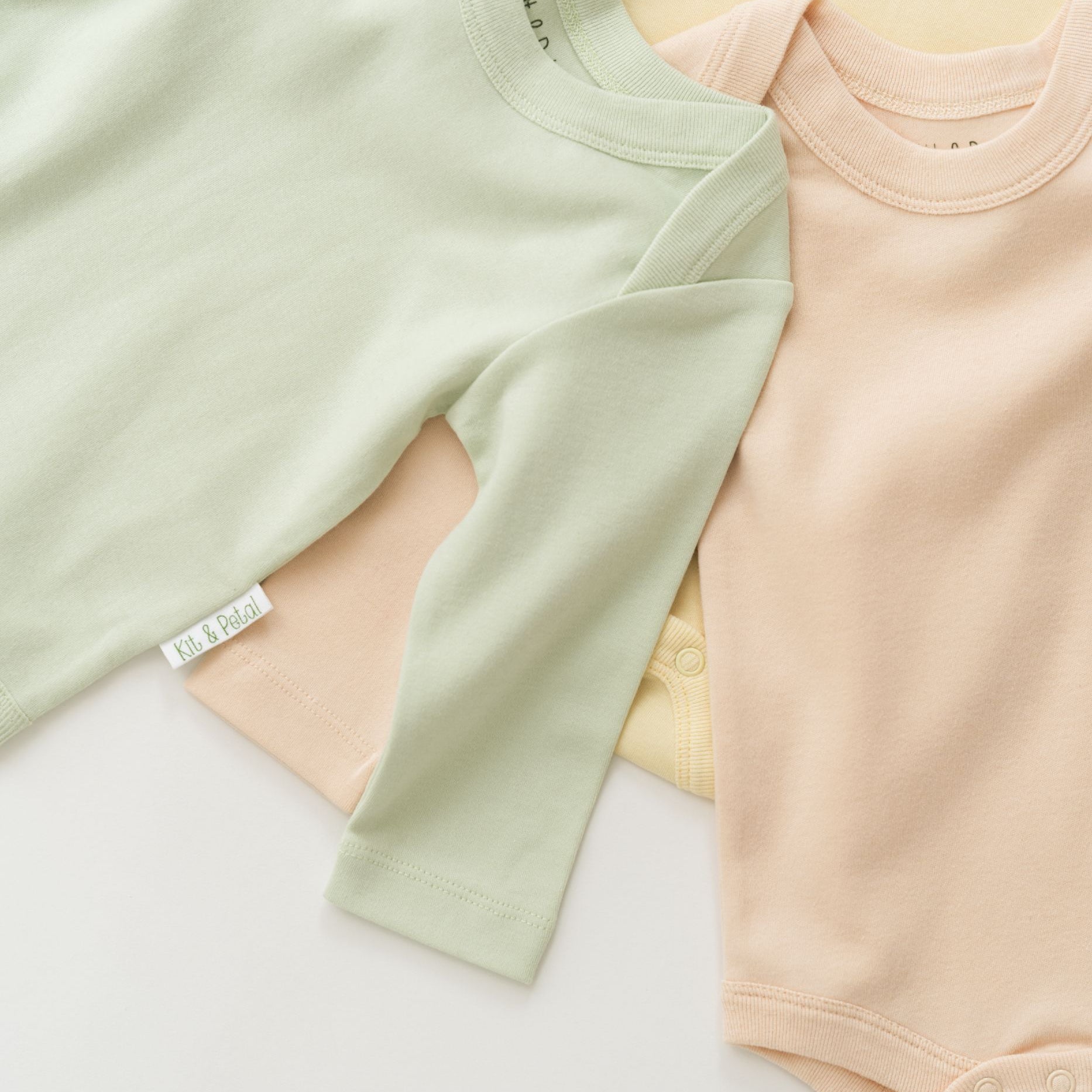 Stack of organic cotton baby long sleeve bodysuits with leafy green on top