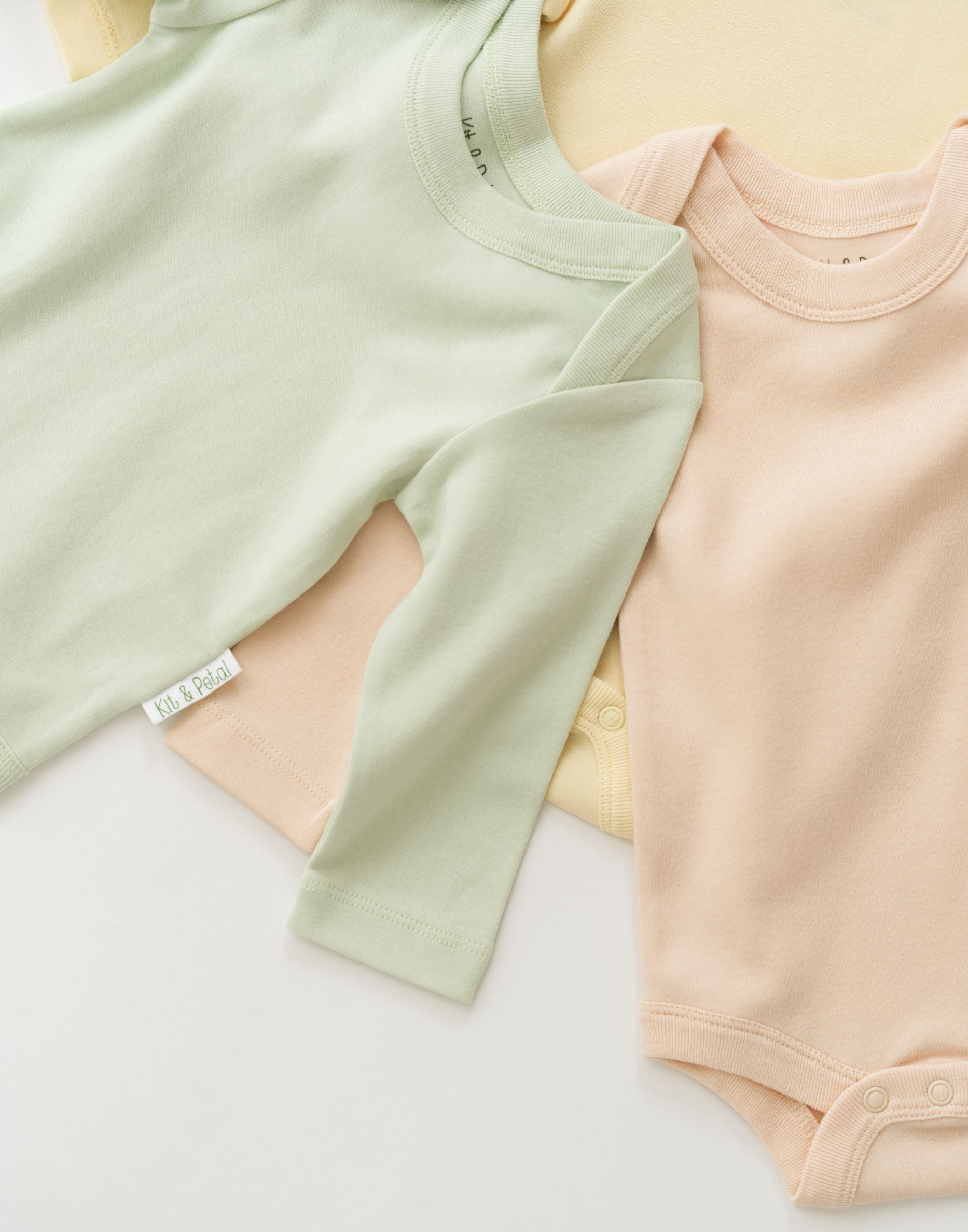 Stack of organic cotton baby long sleeve bodysuits with leafy green on top