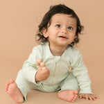 Smiling baby wearing leafy green organic cotton long sleeve romper, holding a toy