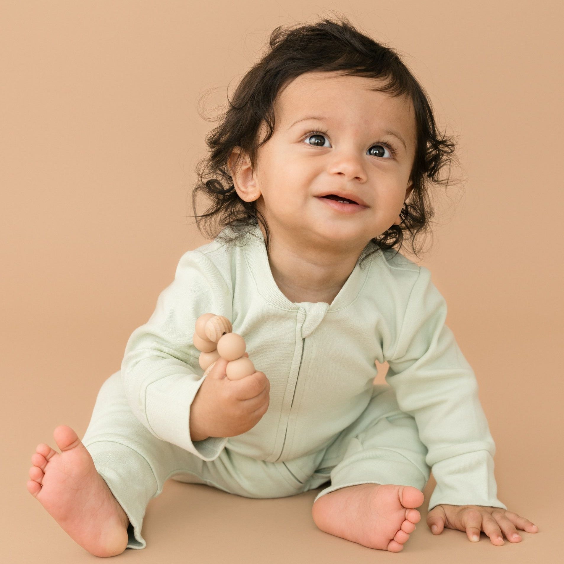 Smiling baby wearing leafy green organic cotton long sleeve romper, holding a toy
