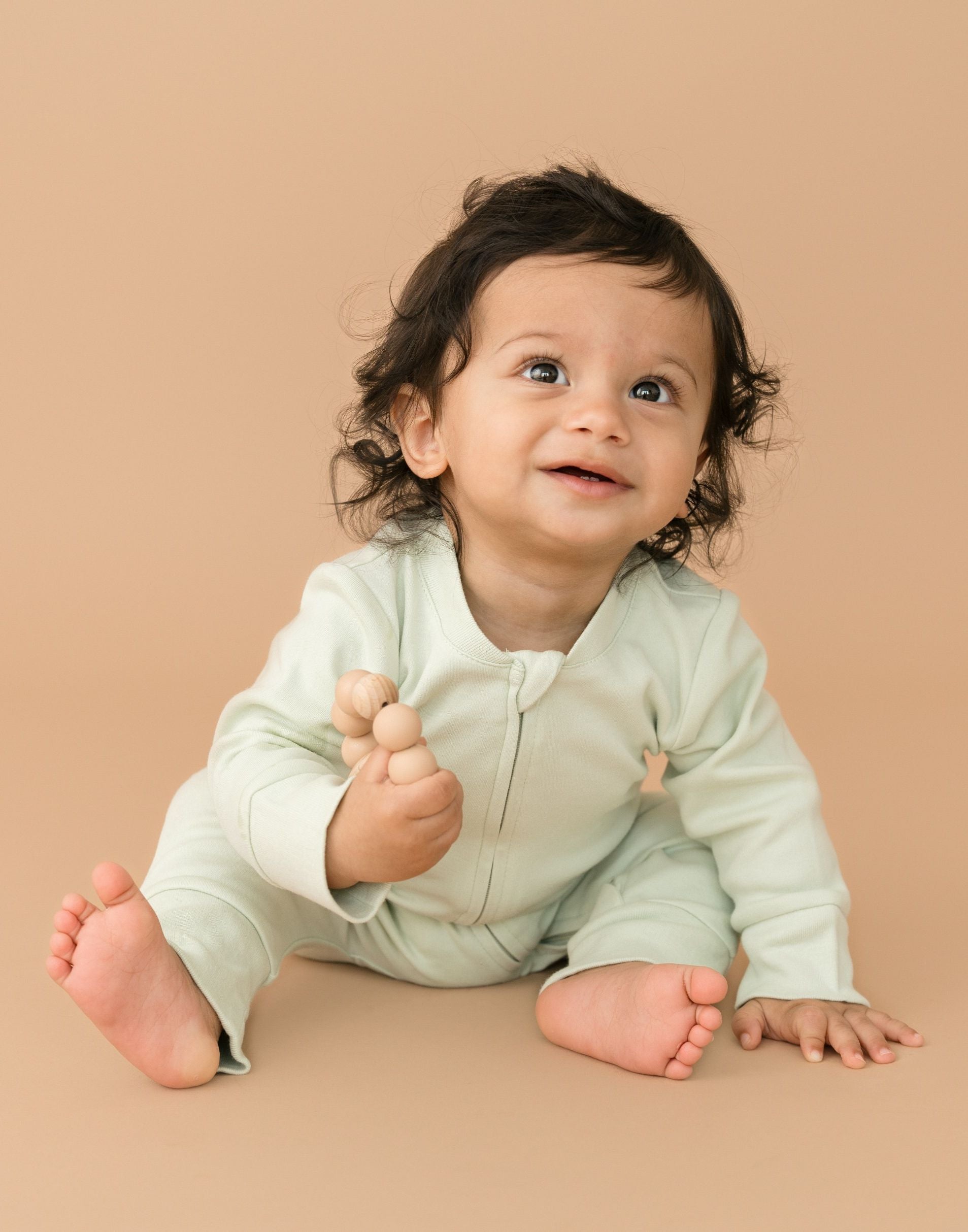 Smiling baby wearing leafy green organic cotton long sleeve romper, holding a toy