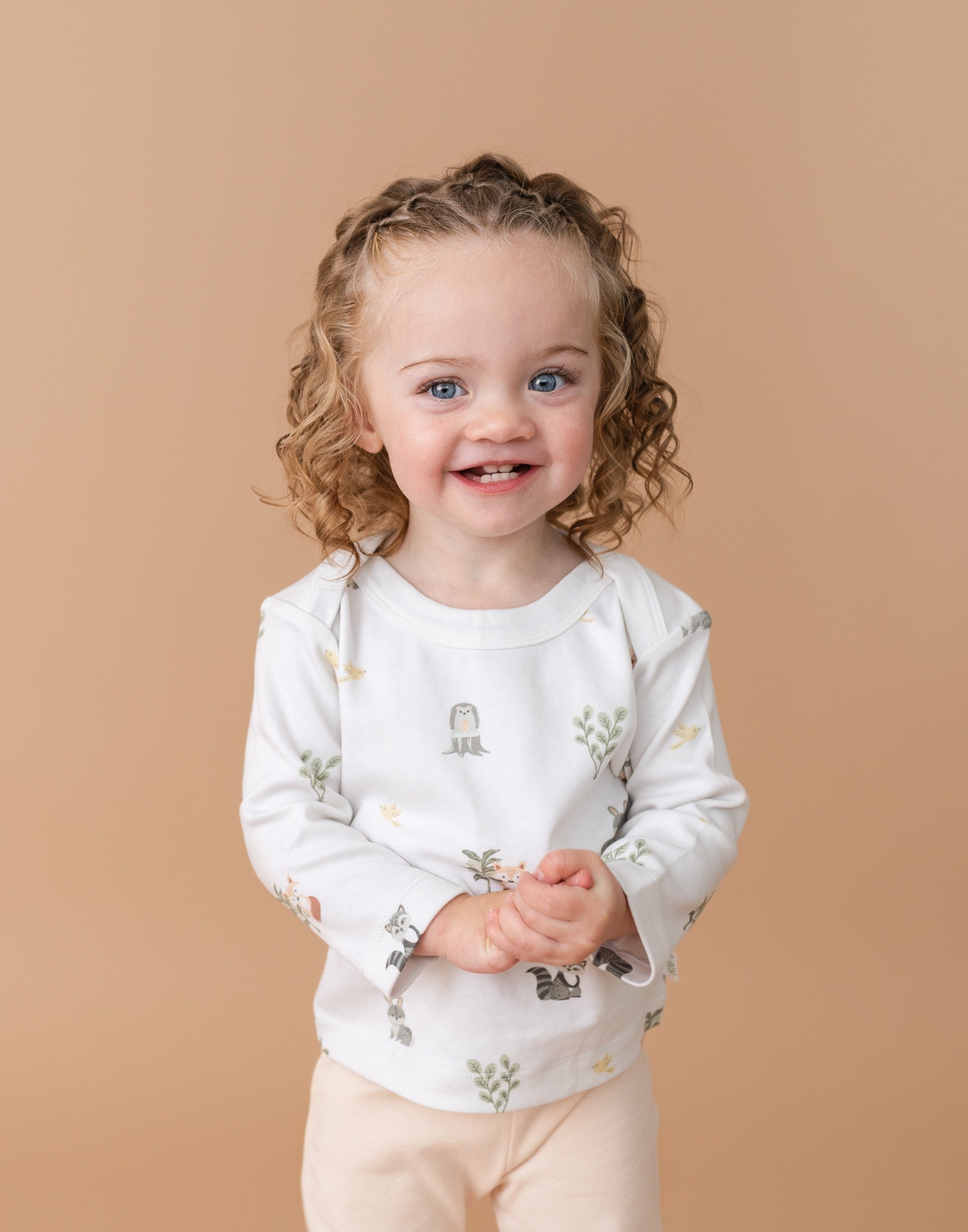 Toddler girl smiling in Forest Friends organic cotton long sleeve shirt and rosy peach fold-over pants