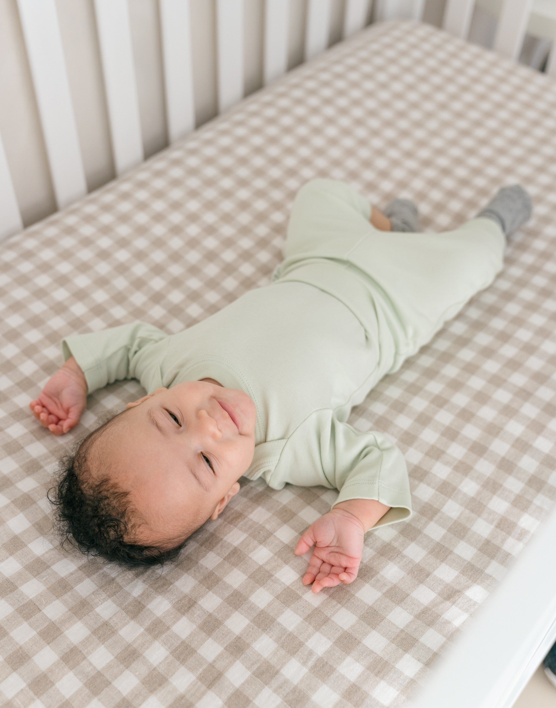 Baby boy wearing a Leafy Green organic cotton long sleeve bodysuit and fold-over pants, laying in a crib.