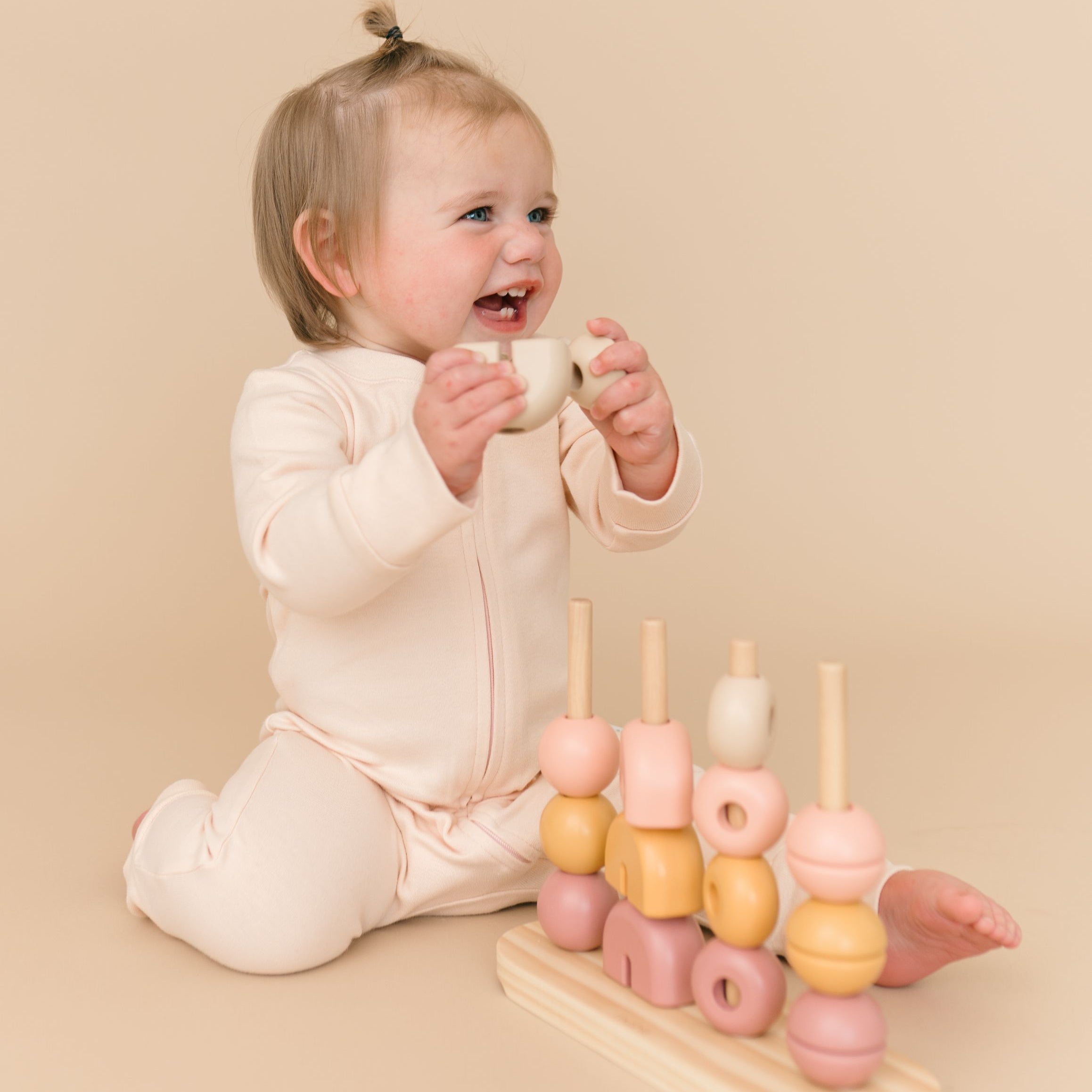 Toddler girl wearing rosy peach organic cotton long sleeve romper, playing with a toy