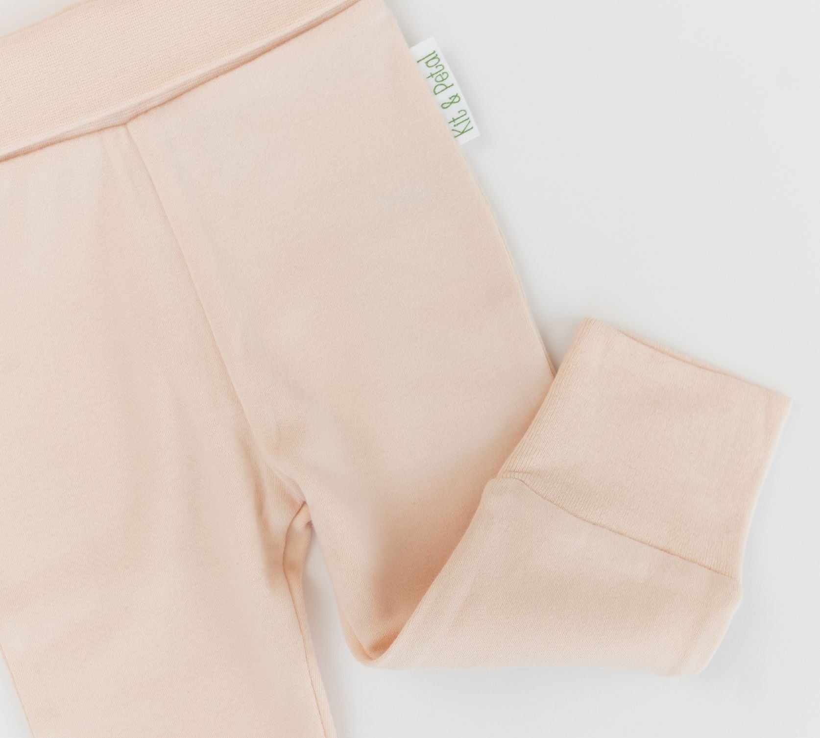 Close-up of soft, wide waistband and hem details on rosy peach organic cotton baby fold-over pants