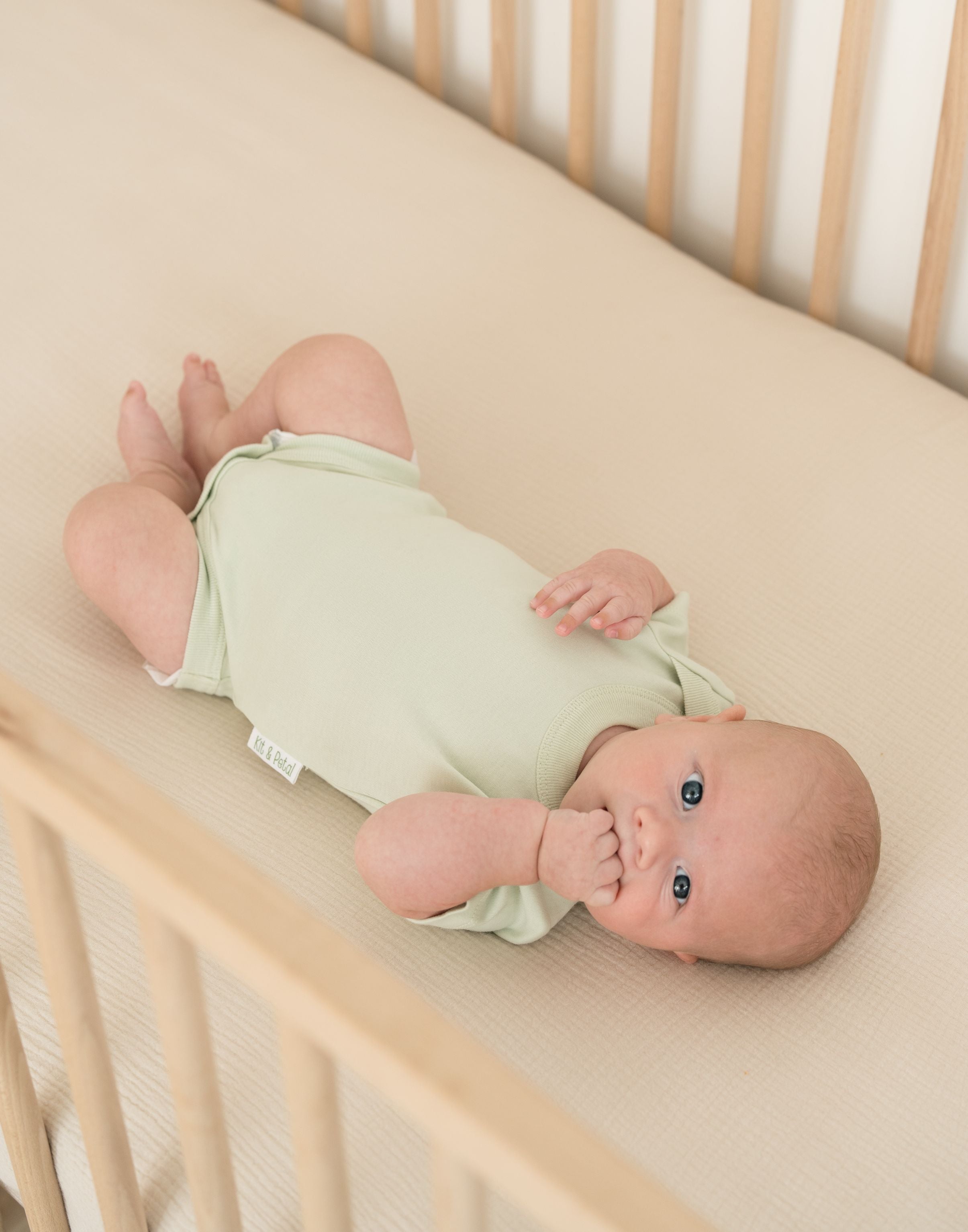 Baby lying in crib wearing leafy green organic cotton short sleeve bodysuit