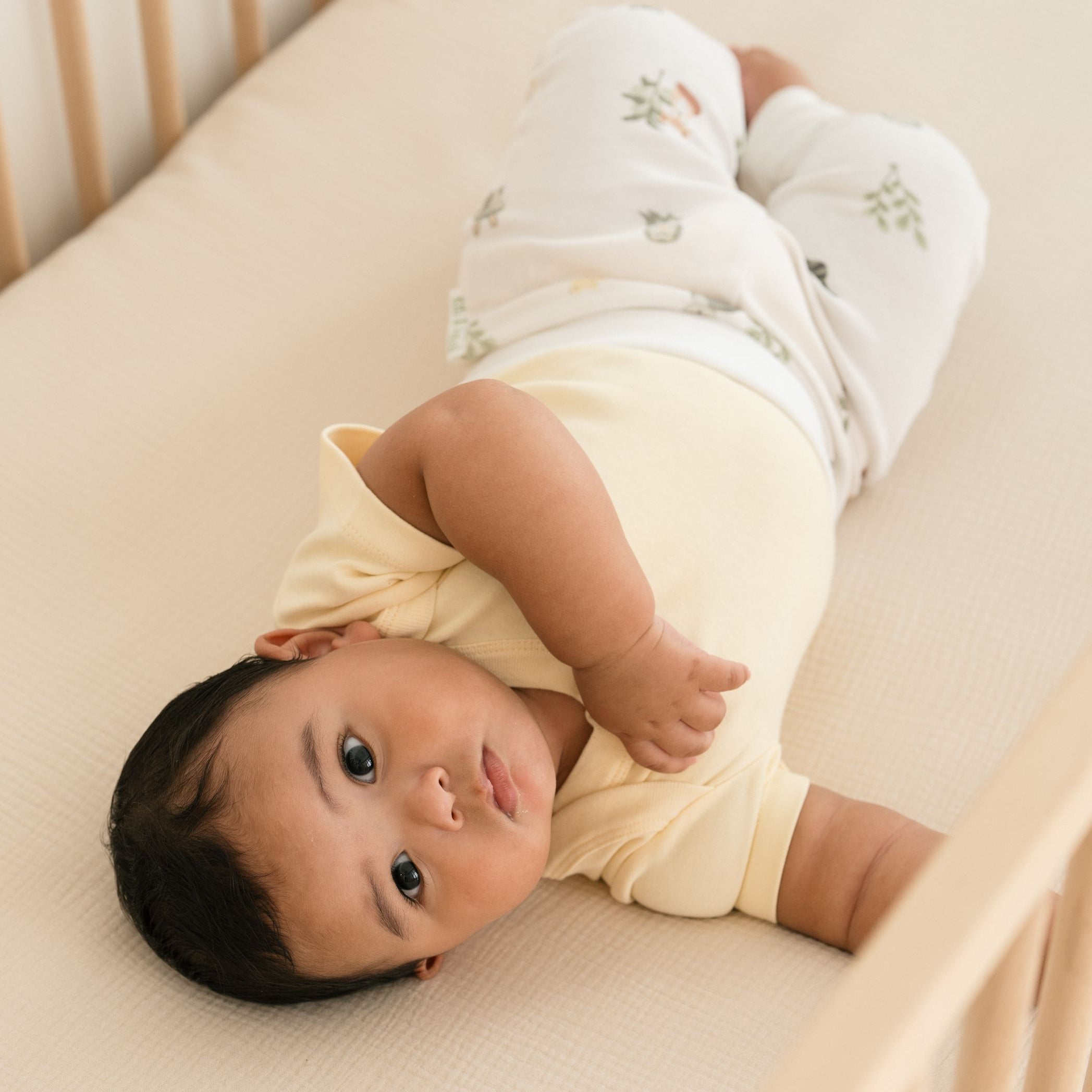 Baby lying in crib wearing sunny yellow organic cotton short sleeve bodysuit and Forest Friends print fold over pants